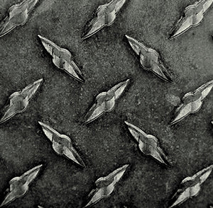 Close-up of dark gray diamond plate metal with raised repeating tread patterns.
