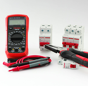 Digital multimeter with red test leads next to several miniature circuit breakers and insulated hand tools on a white background.